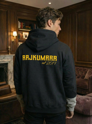 Back view of Rajkumarr hoodie showcasing the yellow logo, worn by a model in an elegant indoor setting.