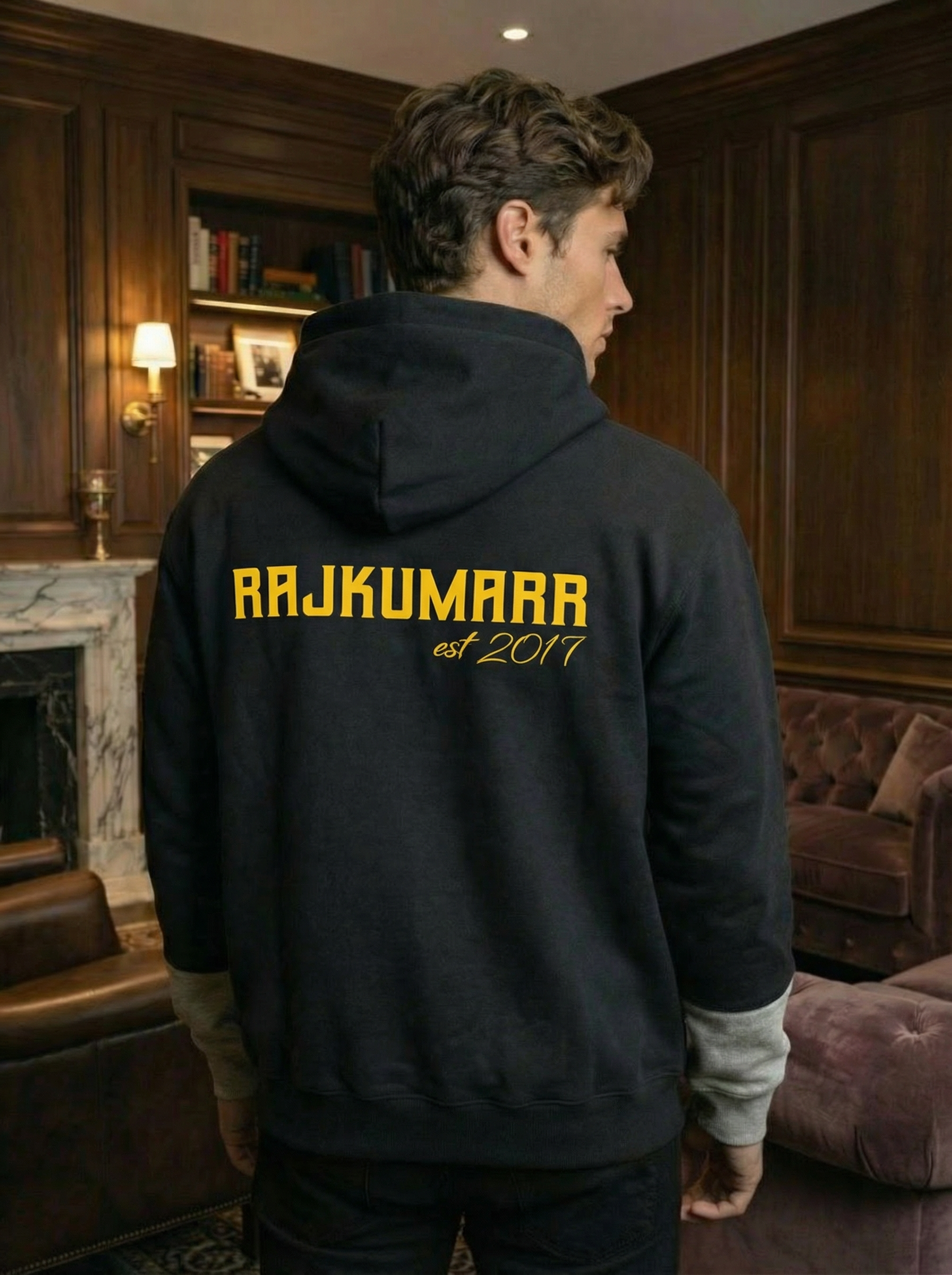 Back view of Rajkumarr hoodie showcasing the yellow logo, worn by a model in an elegant indoor setting.